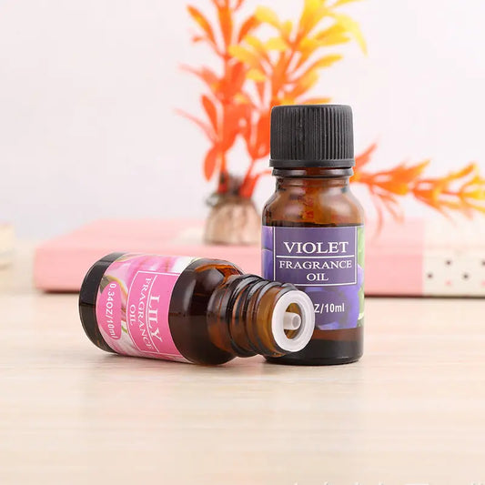Two bottles of fragrance oil, one labeled 'Violet' and the other 'Lilac', on a wooden surface with a blurred background.