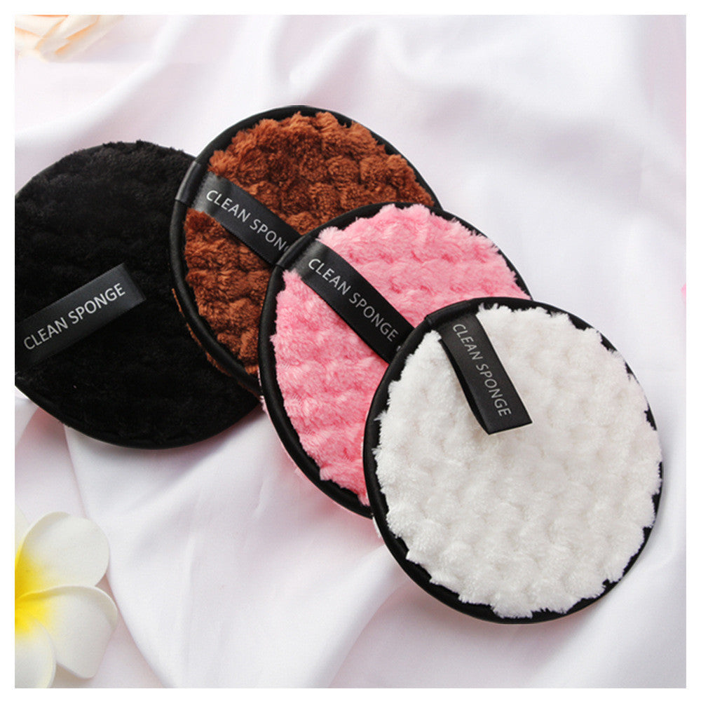 Four round soft clean sponges in black, brown, pink, and white colors on white fabric