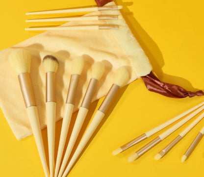 Set of beige makeup brushes with brown ferrules displayed on yellow background with a soft beige pouch