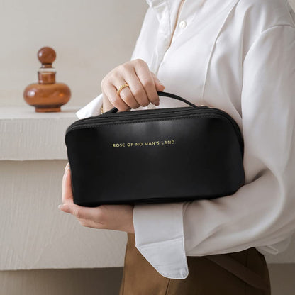 Person holding a black cosmetic bag with 'Rose of No Man's Land' branding.
