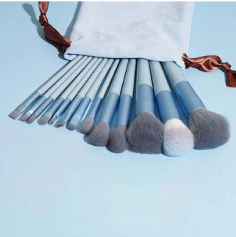 Set of blue makeup brushes with gray bristles in a white pouch on light blue background