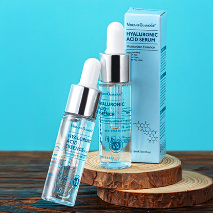 Two Vibrant Glamour Hyaluronic Acid Essence serum bottles with dropper on wooden slices, blue box on blue background
