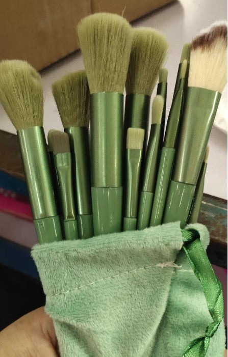 Green-handled makeup brushes with soft bristles held in a light green velvet pouch