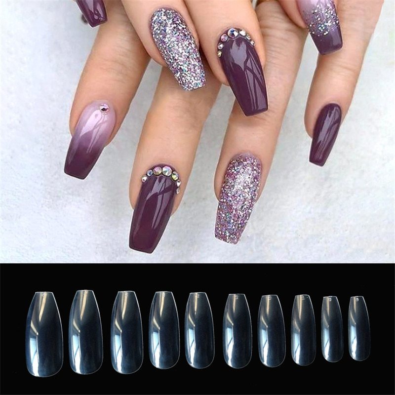 Long coffin-shaped purple acrylic nails with glitter and rhinestone accents, plus clear nail tips display