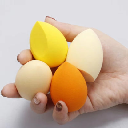 Hand holding four colorful makeup blending sponges in yellow, beige, and orange shades