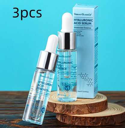 Three Vibrant Glamour hyaluronic acid serum bottles and blue packaging on wooden slices with blue background