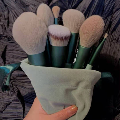 Hand holding a set of green-handled makeup brushes with soft bristles in a light pouch