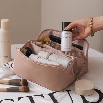 Cosmetic bag with skincare products and makeup brushes on a table.