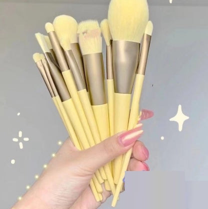 Hand holding a set of yellow-handled makeup brushes with soft bristles against a gray background