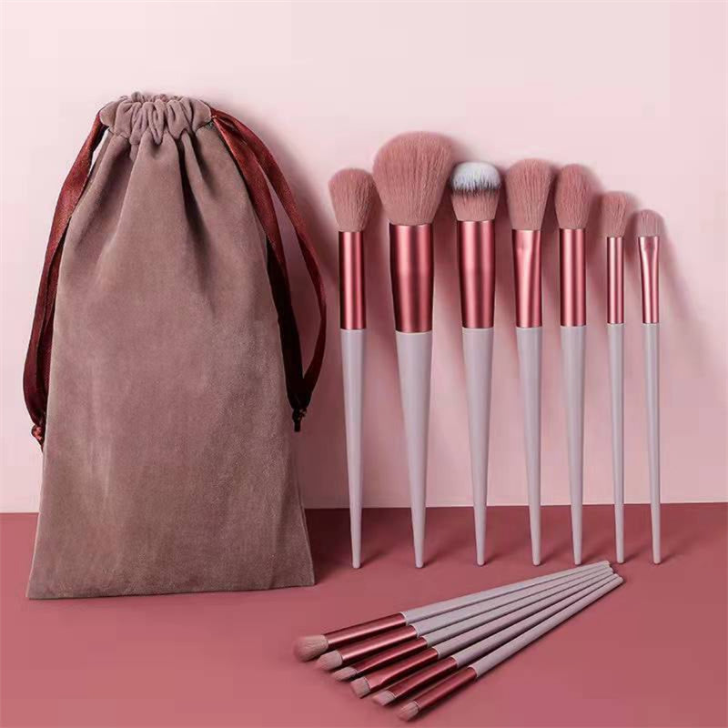 Set of pink and rose gold makeup brushes with soft bristles and matching velvet pouch on pink background