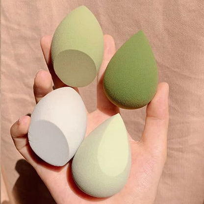 Hand holding four teardrop-shaped makeup blending sponges in shades of green and white
