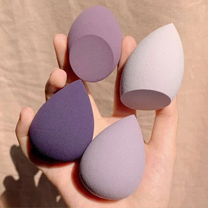 Hand holding four teardrop-shaped makeup blending sponges in various shades of purple and lavender